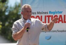 Man speaking on an outdoor stage with a microphone