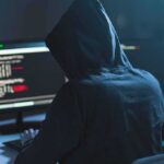 Person in hoodie at dual monitors with code