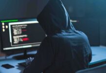 Person in hoodie at dual monitors with code