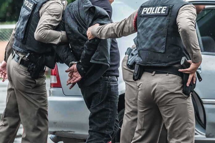 Police officers arresting a person beside a car
