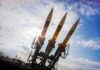 Three surface-to-air missiles on a launcher against a bright sky