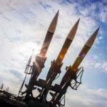 Three surface-to-air missiles on a launcher against a bright sky