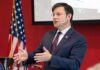 Man in suit speaking at podium with US flag in background