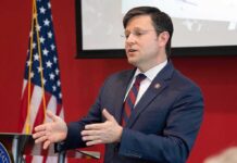 Man in suit speaking at podium with US flag in background
