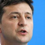 Volodymyr Zelensky speaking in a close-up portrait against a blue background