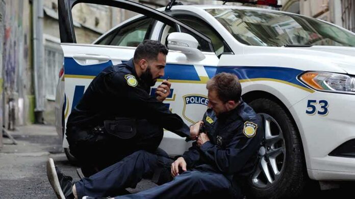 shutterstock_1637627659 Two police officers by a patrol car, one injured and one calling for help