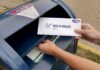 Person mailing a ballot into a blue street mailbox