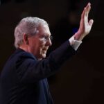 older man in suit raising his hand