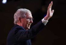 older man in suit raising his hand