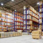 Warehouse aisles with tall blue and orange pallet racks filled with boxes
