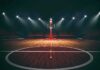 Basketball hoop on an empty indoor court under bright arena lights