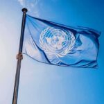 United Nations flag waving on a pole against clear blue sky