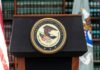 Department of Justice podium with seal in front of bookshelves