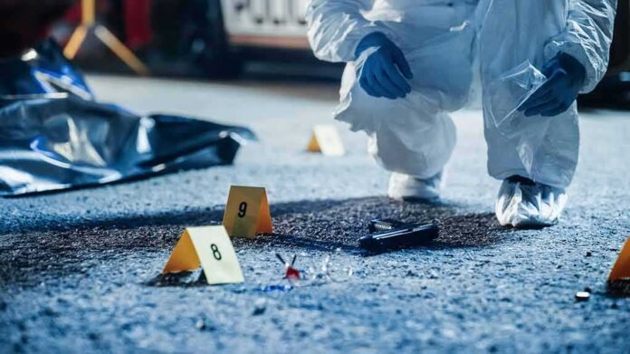 shutterstock_2230642391-2 Forensic investigator examines a crime scene with evidence markers and a handgun