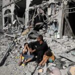 Man with two children sitting amid rubble of a destroyed building