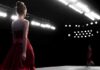 Model in a red dress walking on a runway under bright stage lights