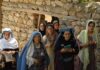 Group of women in traditional clothing standing in front of a stone wall