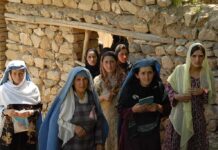 Group of women in traditional clothing standing in front of a stone wall