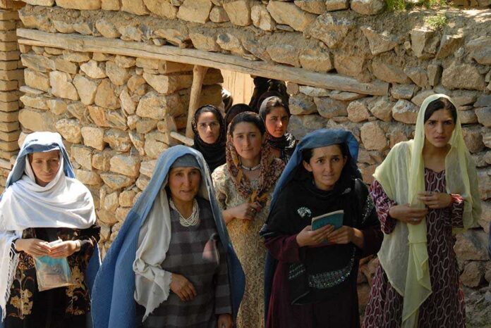 Group of women in traditional clothing standing in front of a stone wall