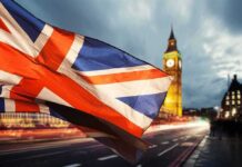 Union Jack flag waving with clock tower in London at dusk