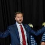 man in suit speaking with arms outstretched