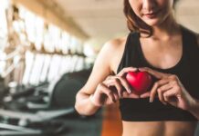 Woman in sportswear holding a red heart-shaped object at the gym