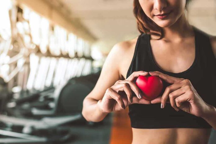 shutterstock_1165619149 Woman in sportswear holding a red heart-shaped object at the gym