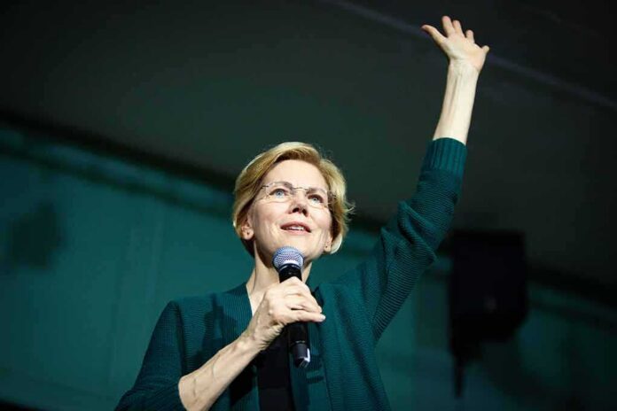 Elizabeth Warren speaking on stage with a microphone, raising one hand