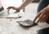 Hands using calculator and laptop over bills