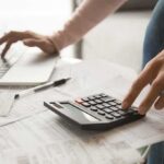 Hands using calculator and laptop over bills