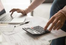 Hands using calculator and laptop over bills