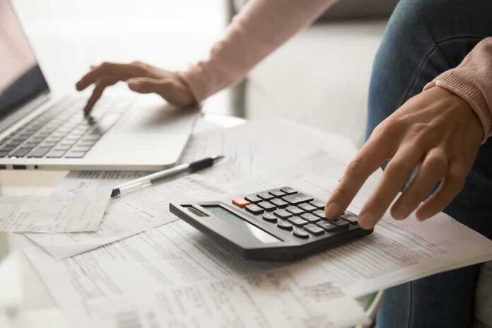 Hands using calculator and laptop over bills