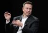 Elon Musk speaking in a black suit against a dark background