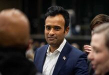 man in a navy suit with a flag pin speaking with people