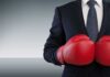 Businessperson in suit wearing red boxing gloves