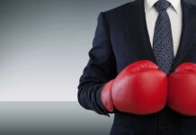 Businessperson in suit wearing red boxing gloves