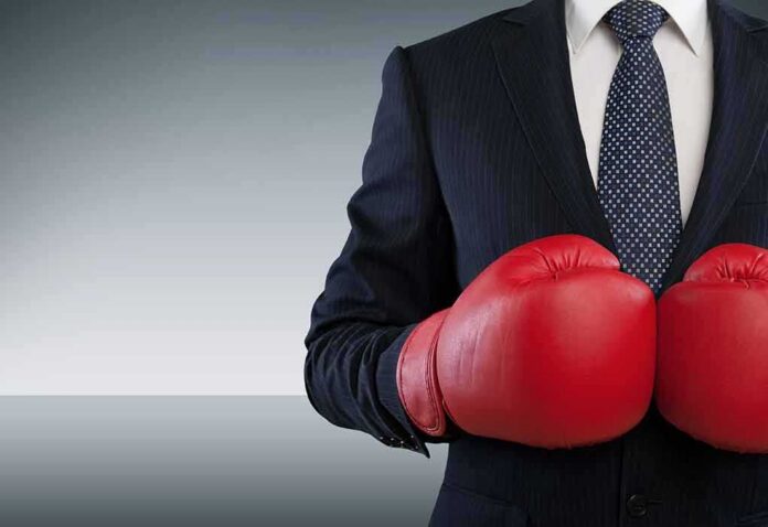Businessperson in suit wearing red boxing gloves