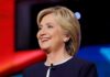 Hillary Clinton smiling in a navy blazer with a lapel microphone