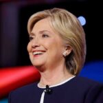Hillary Clinton smiling in a navy blazer with a lapel microphone