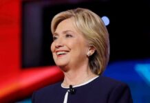 Hillary Clinton smiling in a navy blazer with a lapel microphone