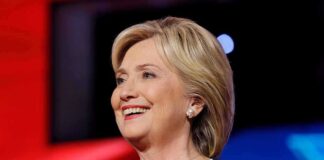Hillary Clinton smiling in a navy blazer with a lapel microphone