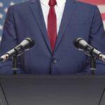 Speaker in suit at podium with microphones