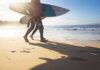 Surfers walking along a sunny beach with boards