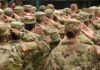 Soldiers in camouflage uniforms salute in formation