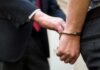 Handcuffed person being escorted by someone in a suit