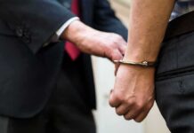 Handcuffed person being escorted by someone in a suit
