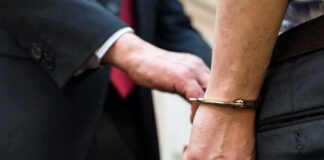 Handcuffed person being escorted by someone in a suit